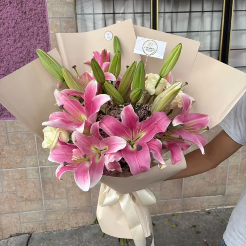 Ramo de lirios rosados y rosas blancas con envoltura en tono neutro de Florería Florae.