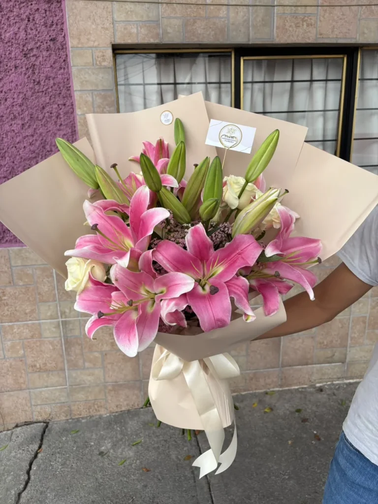 Ramo de lirios rosados y rosas blancas con envoltura en tono neutro de Florería Florae.