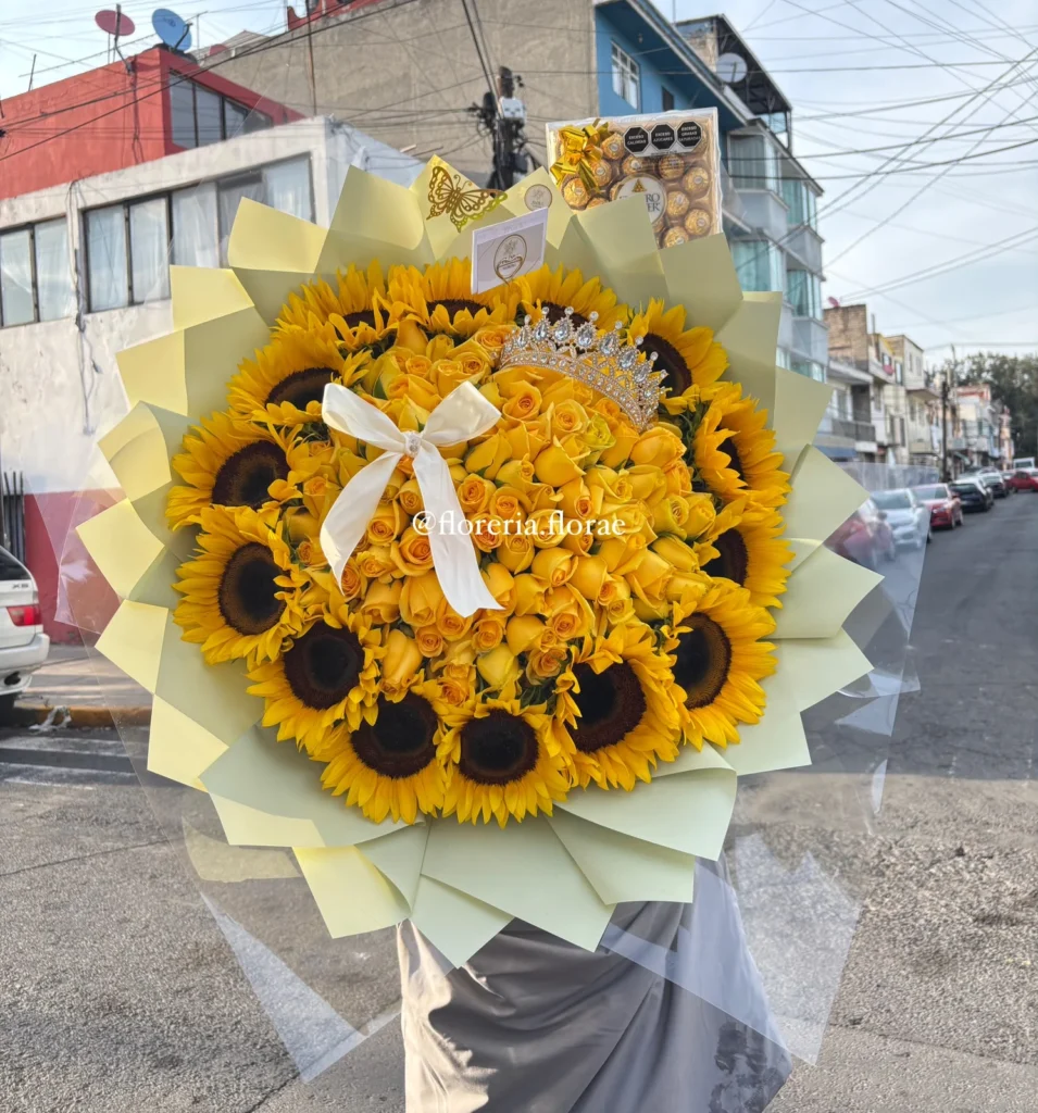 Ramo buchón gigante de 100 rosas amarillas rodeado de girasoles con tiara brillante, globo de corazón rojo, botella de mini vino Riunite y caja de Ferrero Rocher.